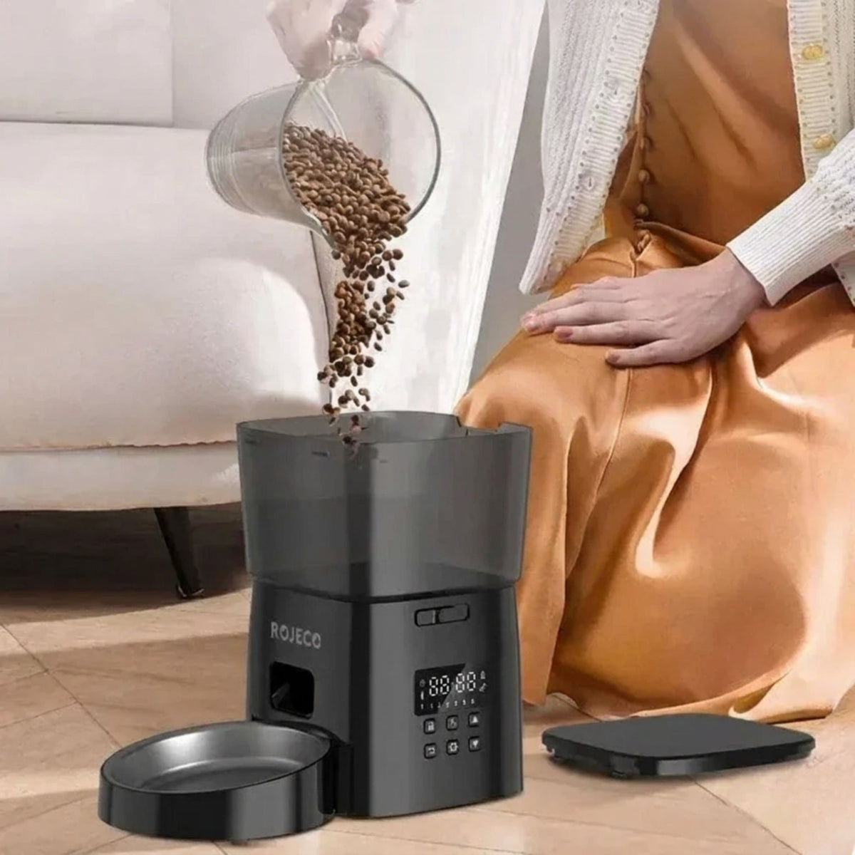 femme qui remplit le réservoir d'un distributeur automatique croquettes pour chat noir avec bol inox amovible posé au sol