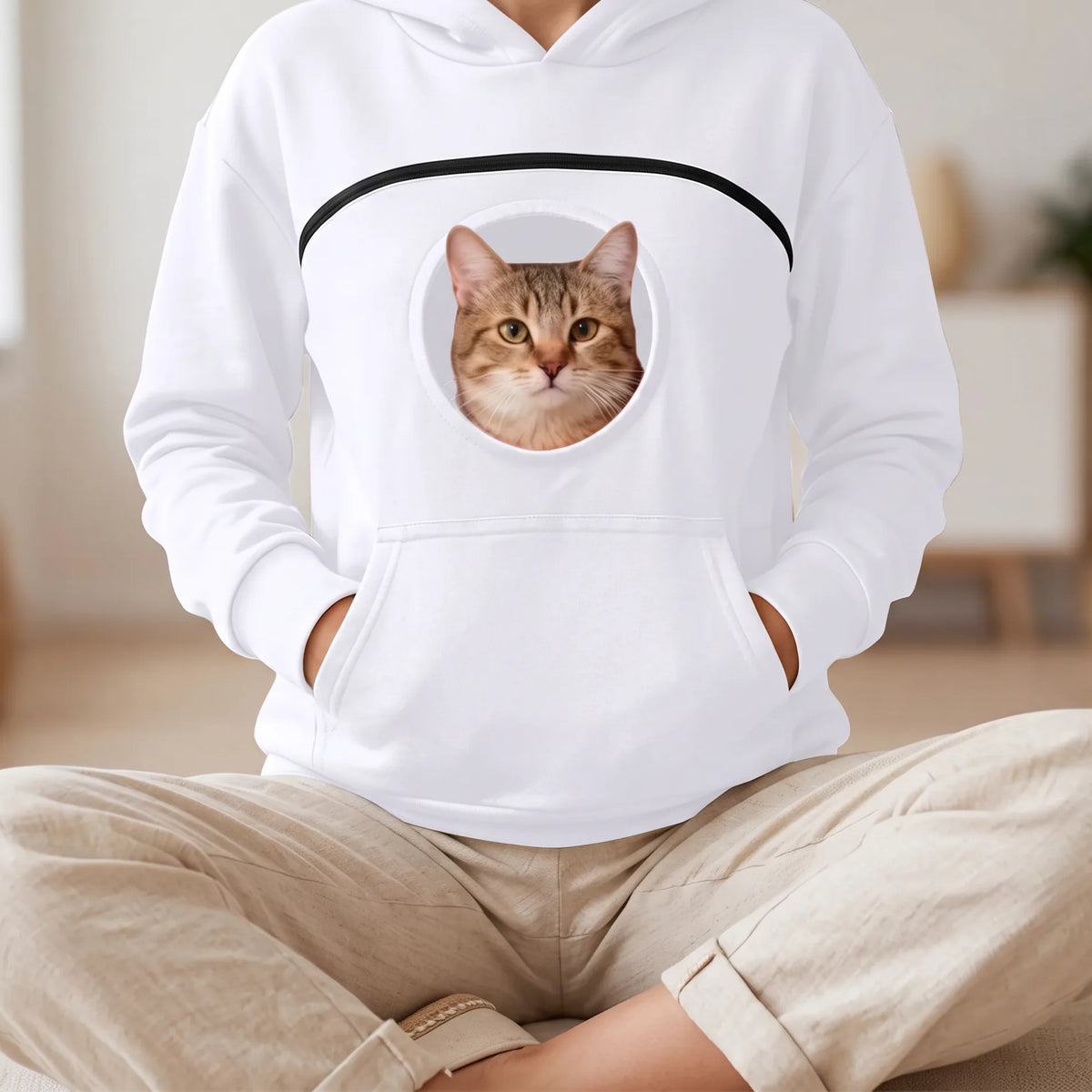 Sweat à capuche blanc porté assise en tailleur, un chat tigré sort la tête du hublot
