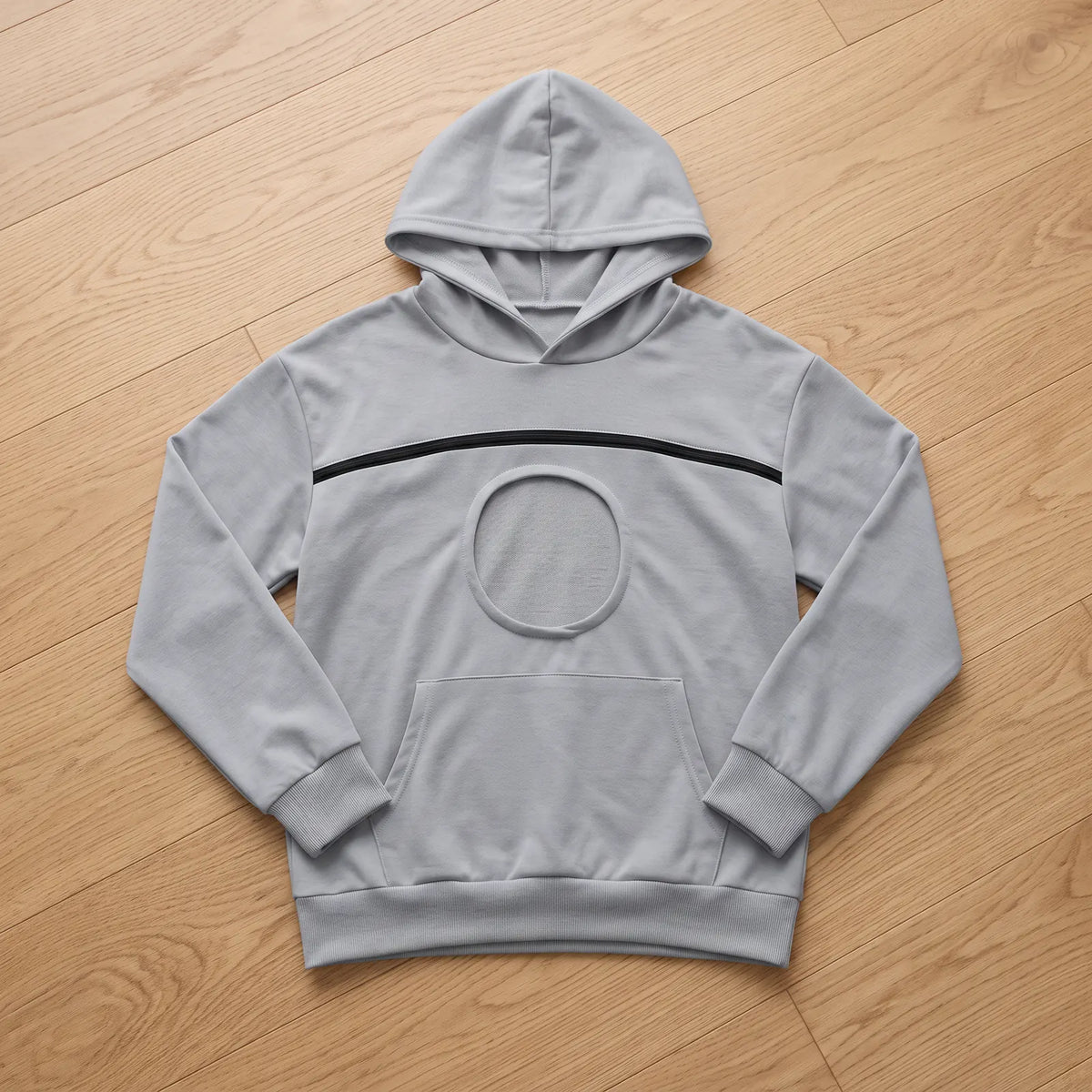 Sweat à capuche gris clair posé à plat, avec son hublot rond et sa poche kangourou
