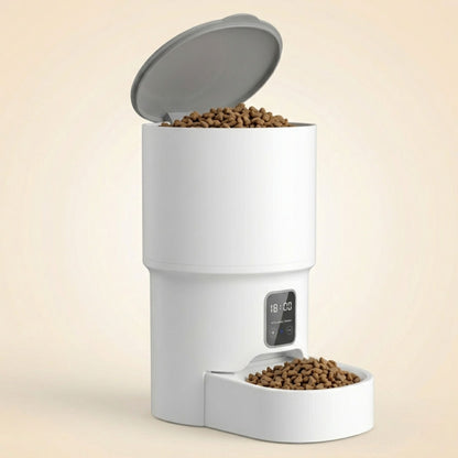 distributeur automatique de croquettes pour chat blanc avec couvercle gris ouvert révélant le réservoir plein de croquettes sèches et bol rempli en bas, fond beige