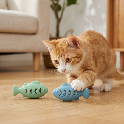 Chaton roux jouant avec deux jouets poisson distributeurs de croquettes en silicone – coloris vert mint et bleu – sur parquet clair, ambiance intérieur cosy