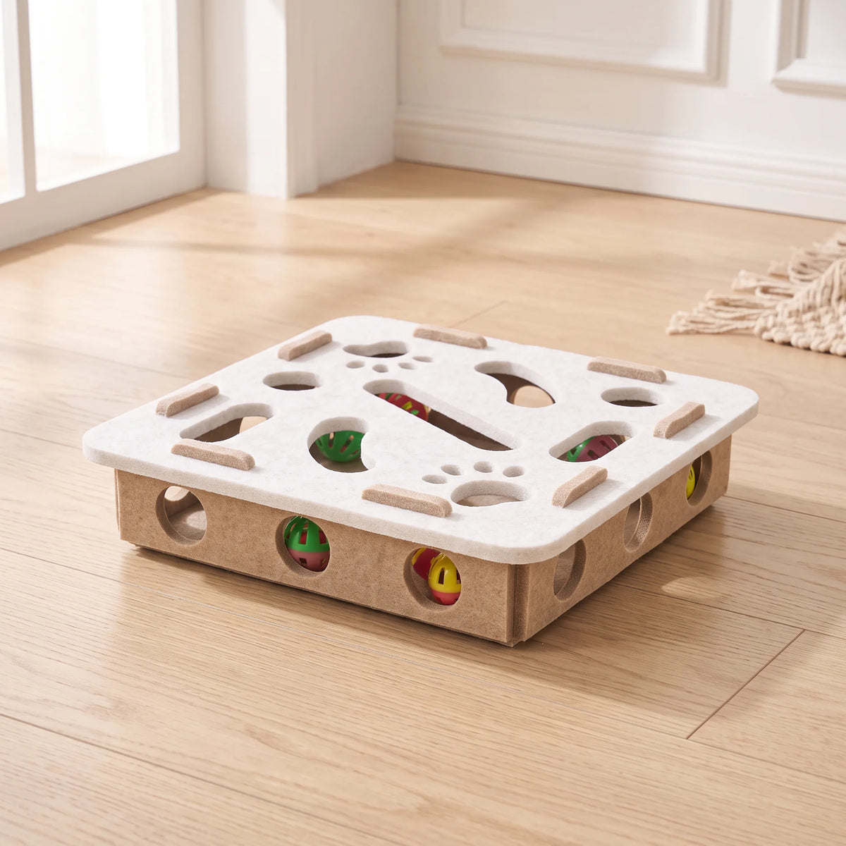 Jouet puzzle pour chat au plateau carré ivoire sur caisson beige, balles colorées visibles à l'intérieur