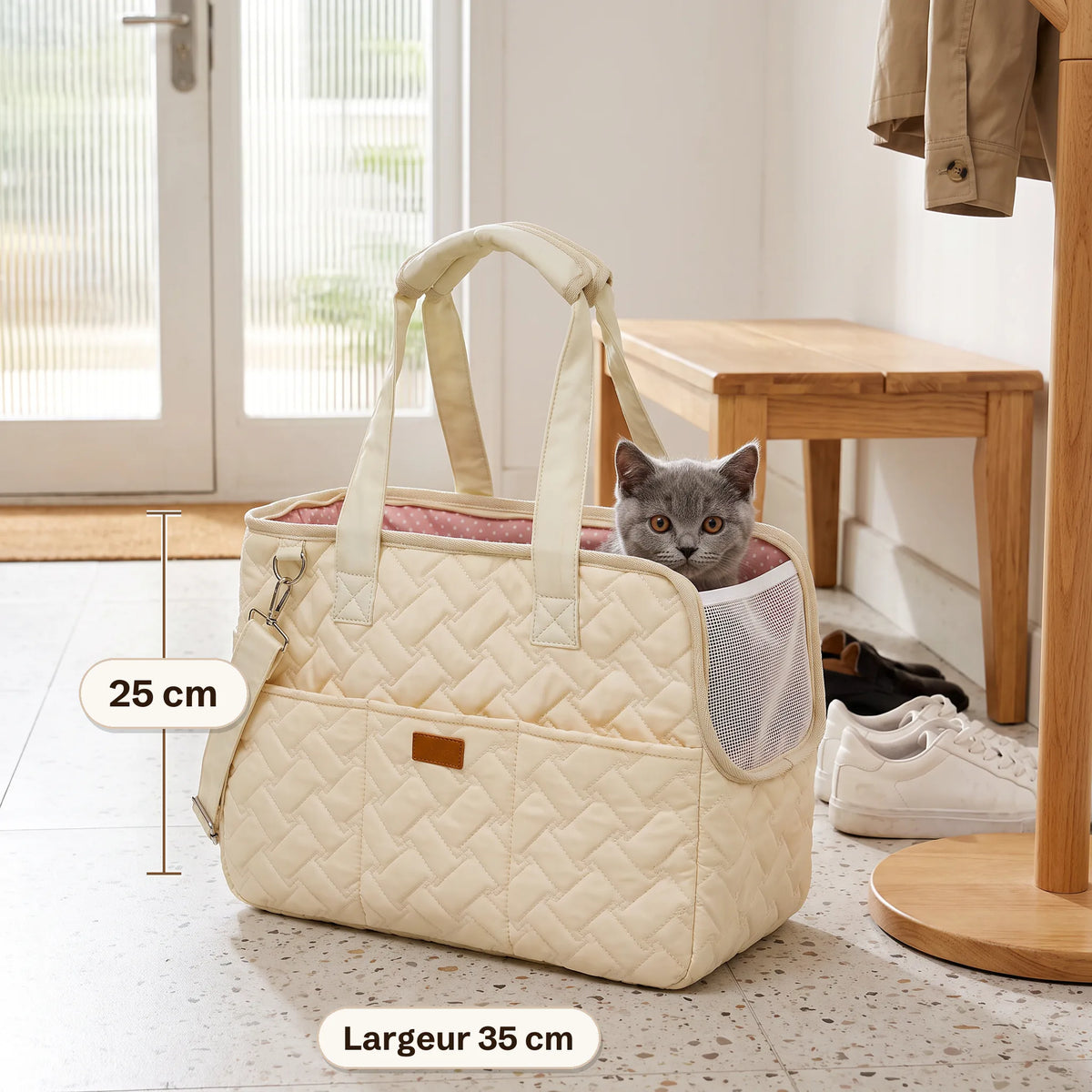 Sac de transport matelassé crème de 25 cm de haut et 35 cm de large posé dans une entrée, un chaton gris qui passe la tête