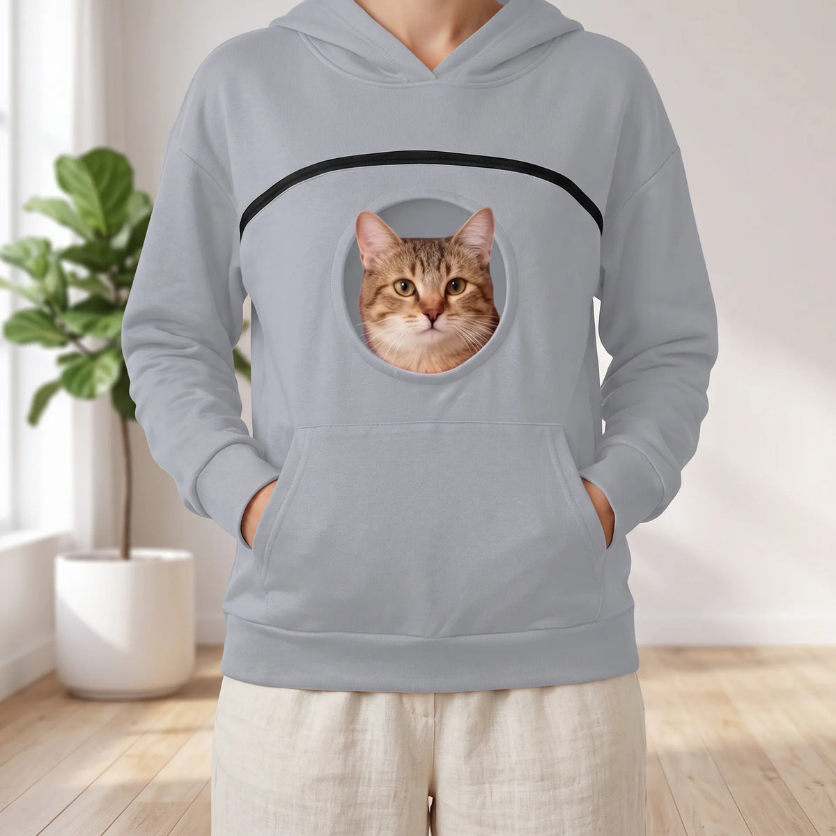 Sweat à capuche gris clair porté, un chat tigré passe la tête par le hublot rond