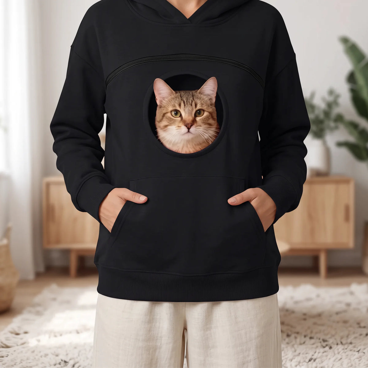 Sweat à capuche noir porté, mains dans la poche kangourou, chat tigré au hublot