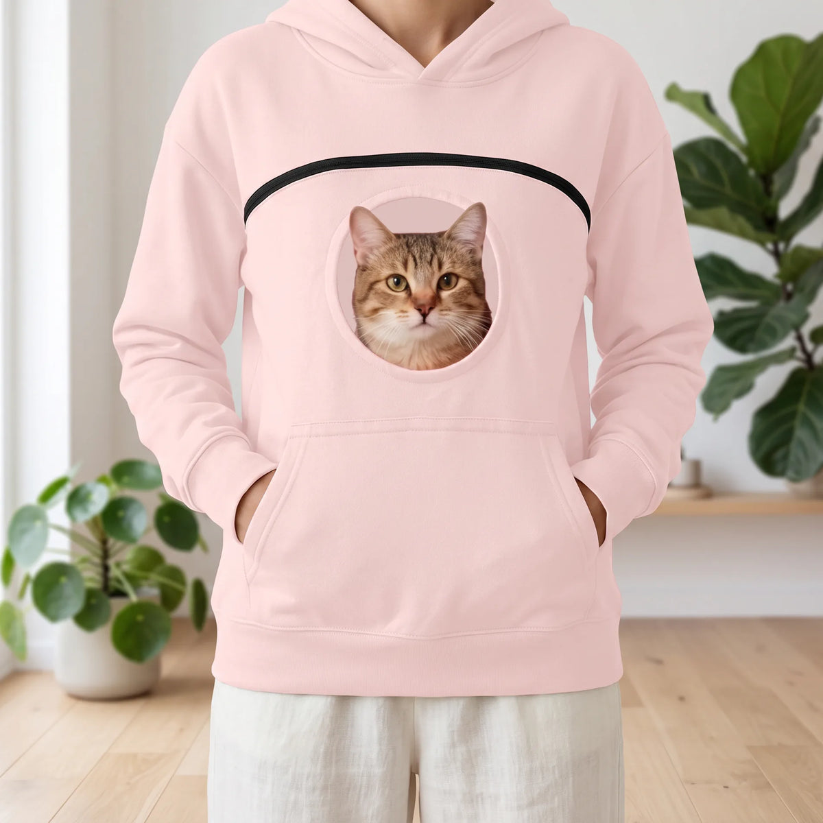 Sweat à capuche rose pâle porté, un chat tigré regarde par le hublot de la poche