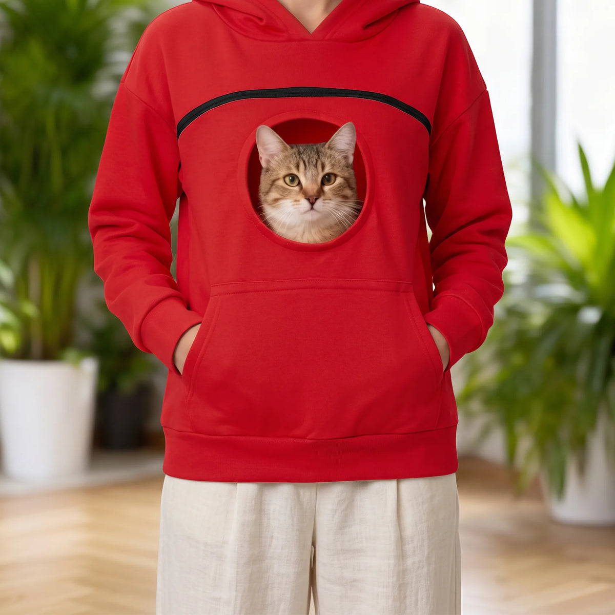 Sweat à capuche rouge porté avec un pantalon en lin, chat tigré au hublot de la poche
